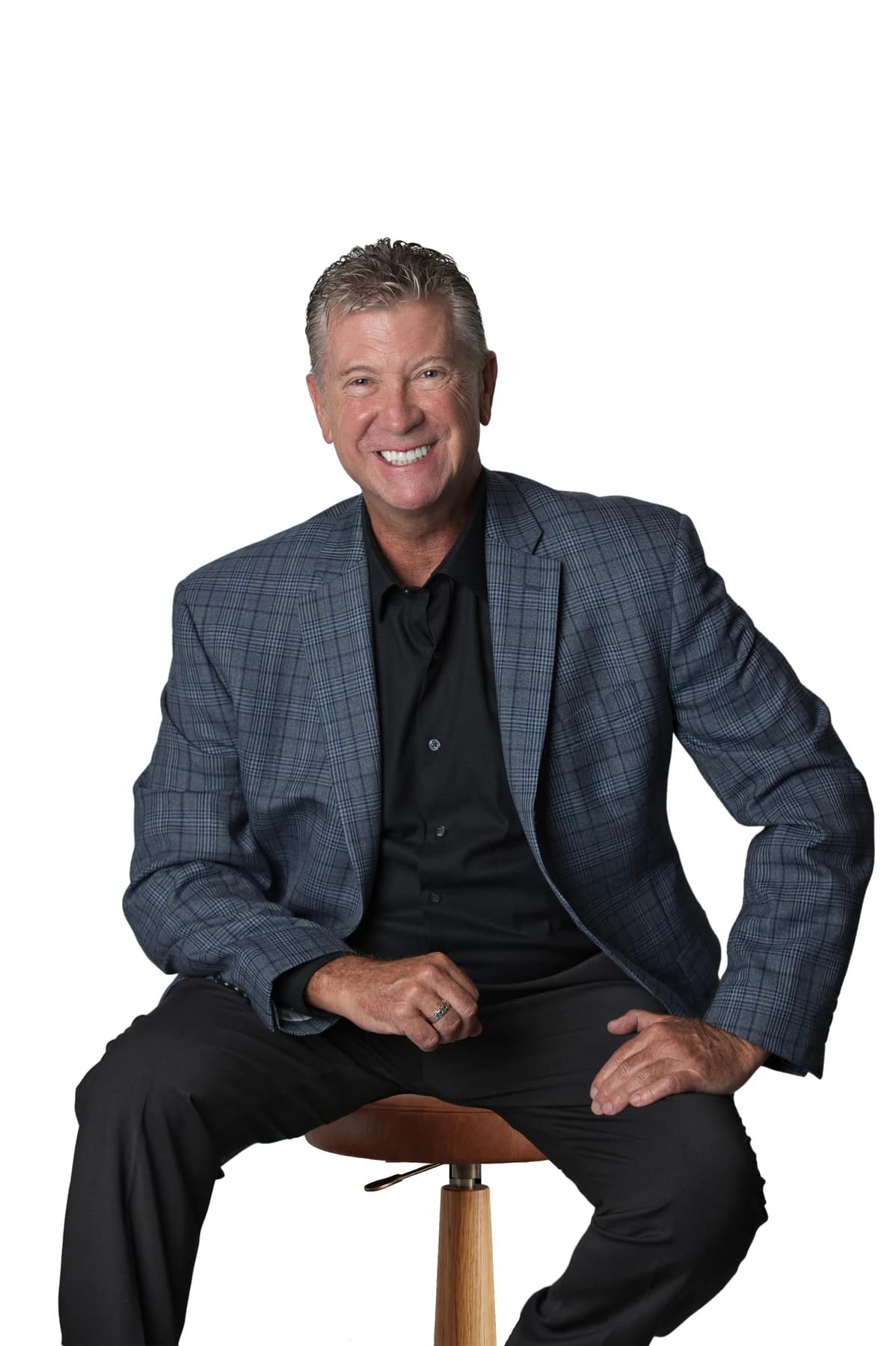 Bob Crews seated on a stool in a blue checked jacket and black shirt